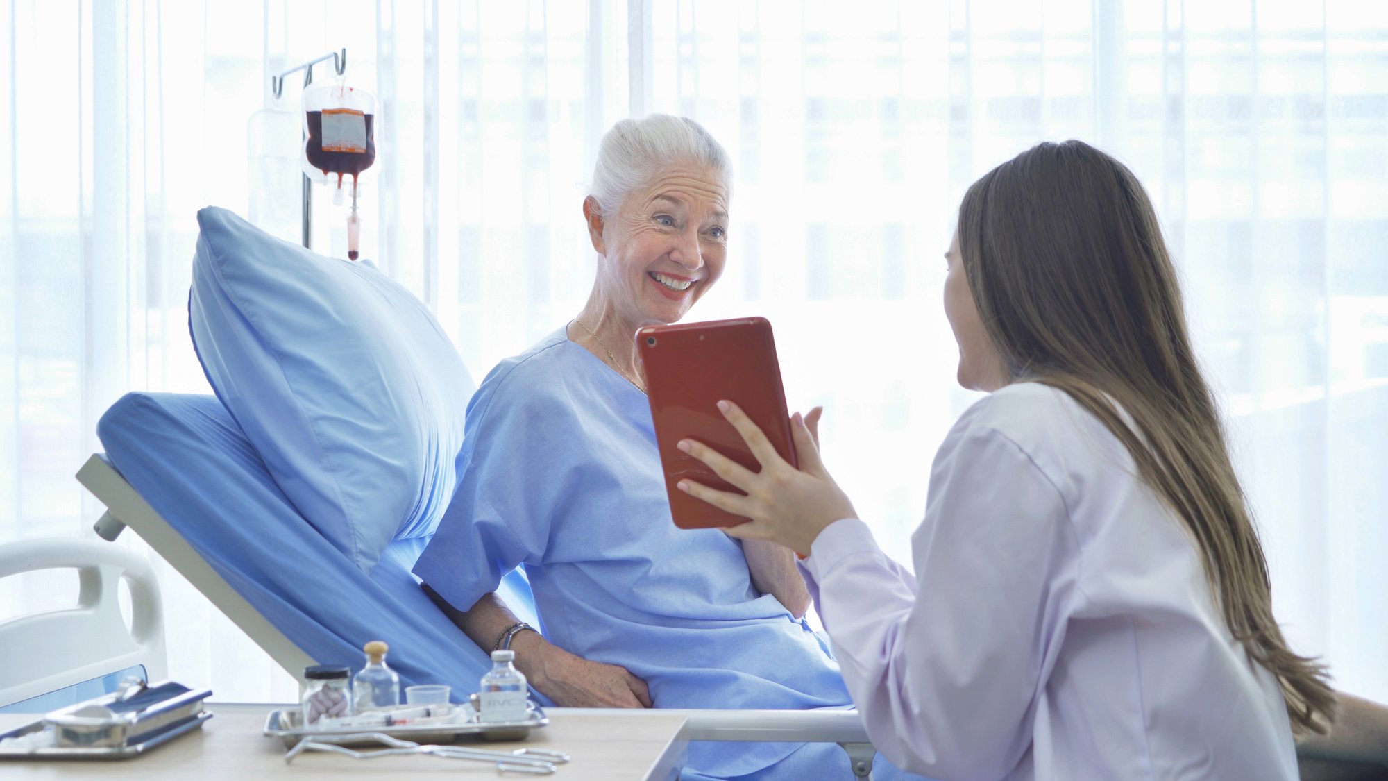 Doctor showing a smiling, female patient in a hospital bed a tablet device