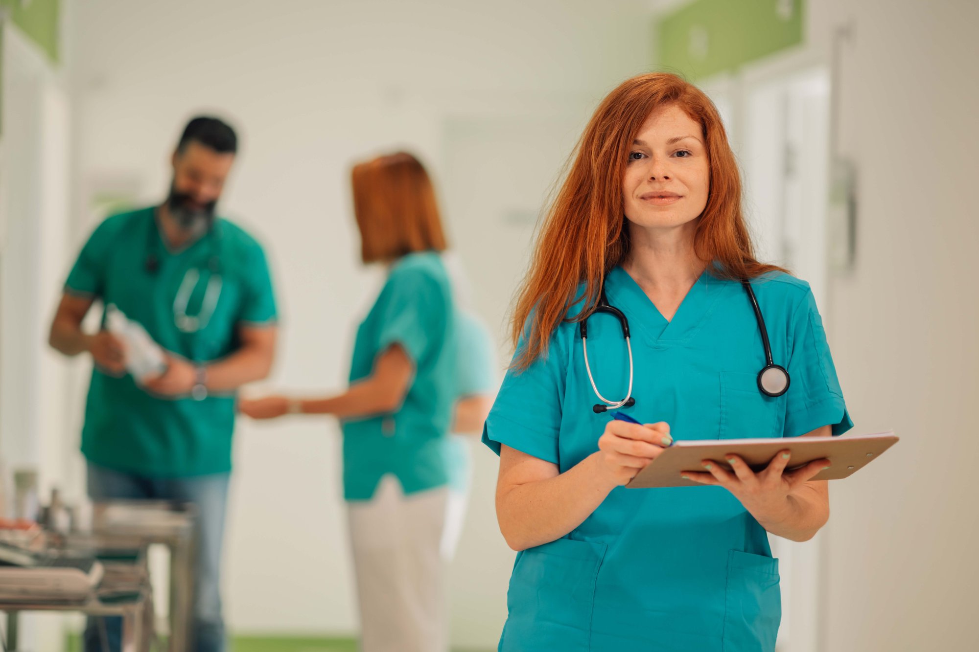 nurse holding clipboard smiling with two nurses in the background